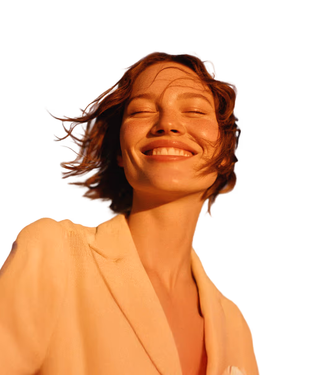 Close-up of a smiling woman with short hair wearing a beige jacket in warm sunlight.